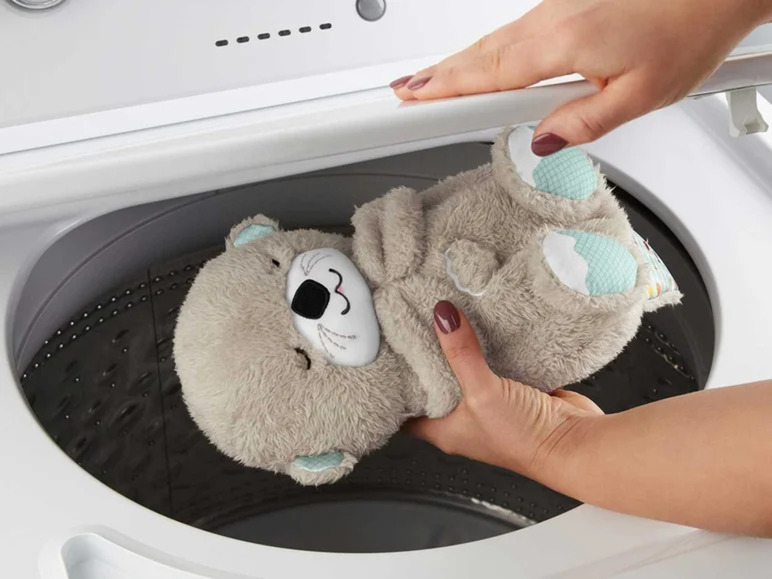 Een grijze knuffeldier in de vorm van een otter wordt in een wasmachine gestopt.