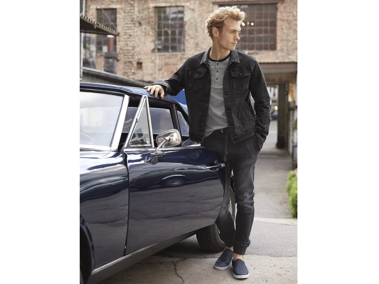 Man in een spijkerjack en jeans, leunend tegen een klassieke auto.