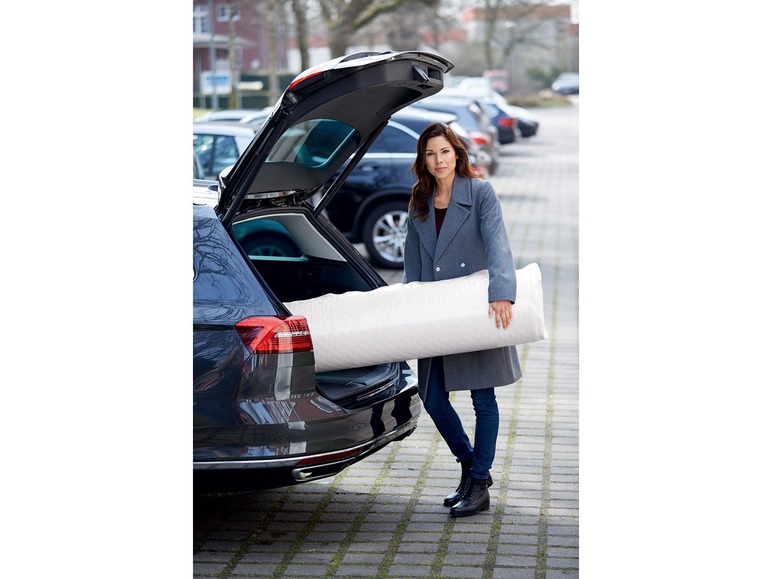 Een vrouw laadt een matras in de kofferbak van een auto.