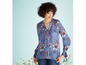 Vrouw met lang, gekruld haar draagt een blauwe blouse met bloemenprint.