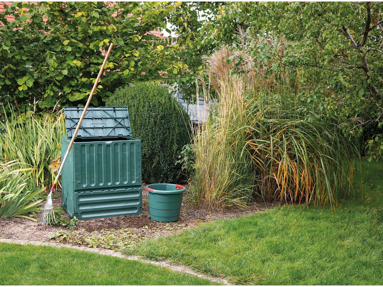 Compostbak, emmer en hark in een tuin.