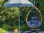 Een hangstoel met kussen en een parasol met franjes in een tuin.