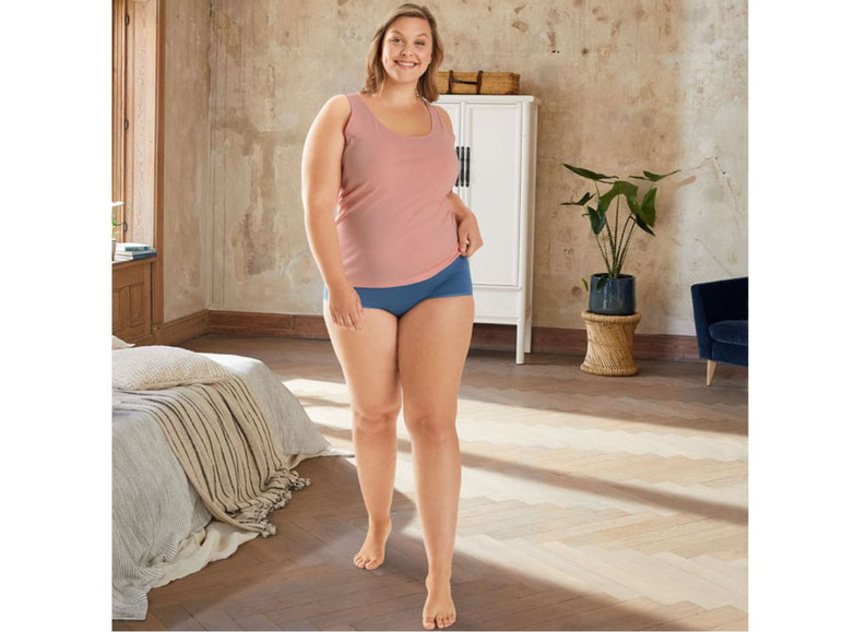 Een vrouw draagt een roze tanktop en blauwe onderbroek.