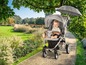 Een baby in een grijze wandelwagen met parasol op een pad in een tuin.