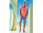 Een man draagt een roze polo, blauwe shorts en een pet met surfplanken op de achtergrond.