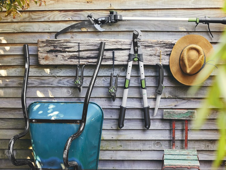 Een blauwe kruiwagen, snoeischaar en een zaag op een houten muur.