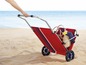 Een rode strandwagen met een mand en handdoek, klaar voor een dagje aan het strand.