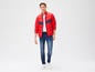 Man draagt een rode jas met blauwe details en blauwe jeans.