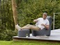 Een man zit op een grijze loungestoel en een bijpassende poef op een houten terras.