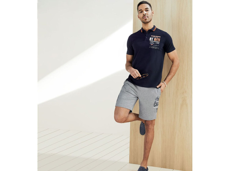 Man draagt een blauwe polo met korte mouwen en grijze korte broek.