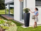 Een vrouw giet water uit een gieter in een regenwaterton voor een modern huis.
