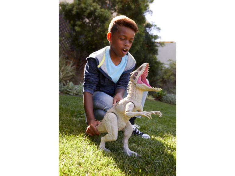 Een jongen speelt met een Jurassic World Indoraptor-actiefiguur in de tuin.