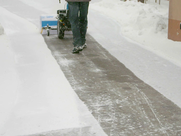 Een persoon die sneeuw opruimt met een kleine sneeuwschuiver.