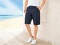 Man draagt blauwe cargo shorts en witte sneakers aan het strand.
