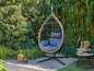 Een hangstoel met een houten frame in een tuin met groene planten.