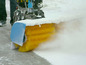 Een blauwe sneeuwruimer met gele borstels verwijdert sneeuw van een pad.