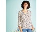 Een vrouw draagt een witte blouse met bloemenprint en jeans.
