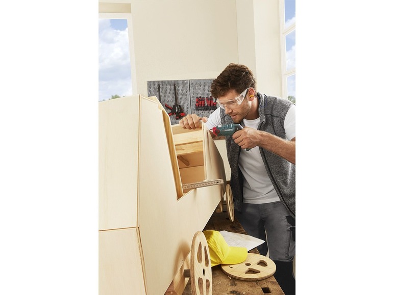 Een man gebruikt een Parkside schroevendraaier om een houten speelgoedauto te bouwen.