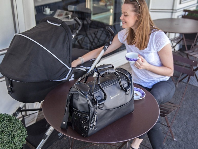 Een zwarte Babybjörn luiertas en een buggy op een terras.