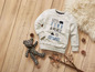 Een wit sweatshirt met de tekst 'Let's find a place to explore' en een teddybeer op een houten vloer.