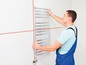 Een man hangt een handdoekradiator op een witte muur