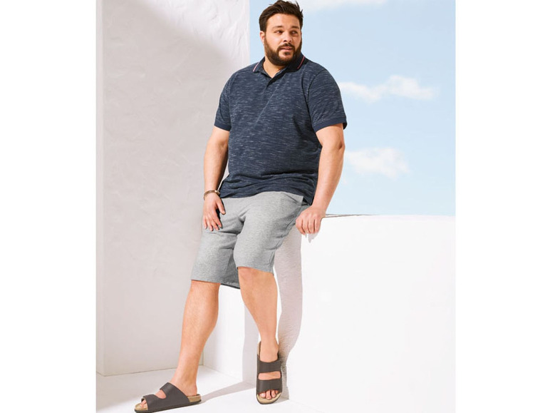 Man draagt een blauwe polo, grijze shorts en sandalen.
