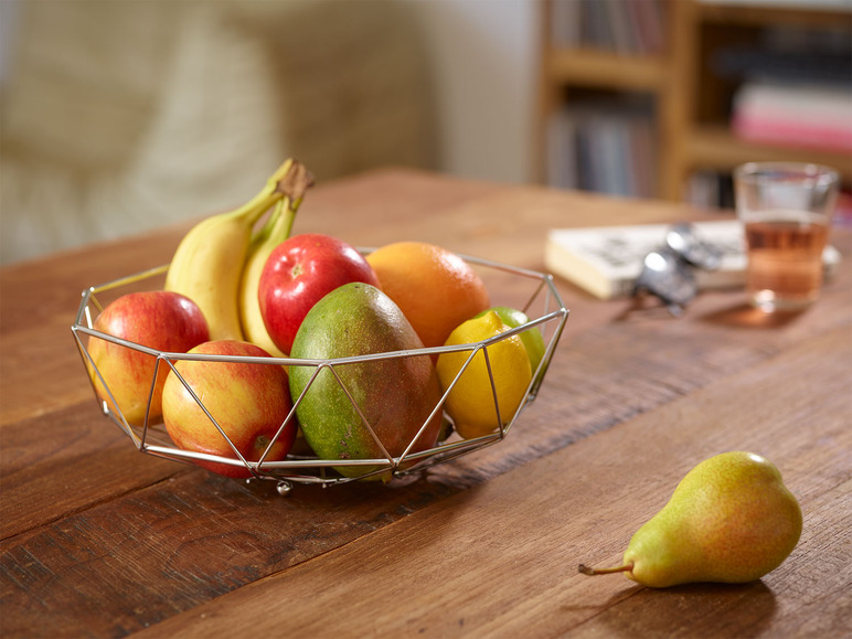 Een metalen fruitmand met appels, bananen, mango en citroen