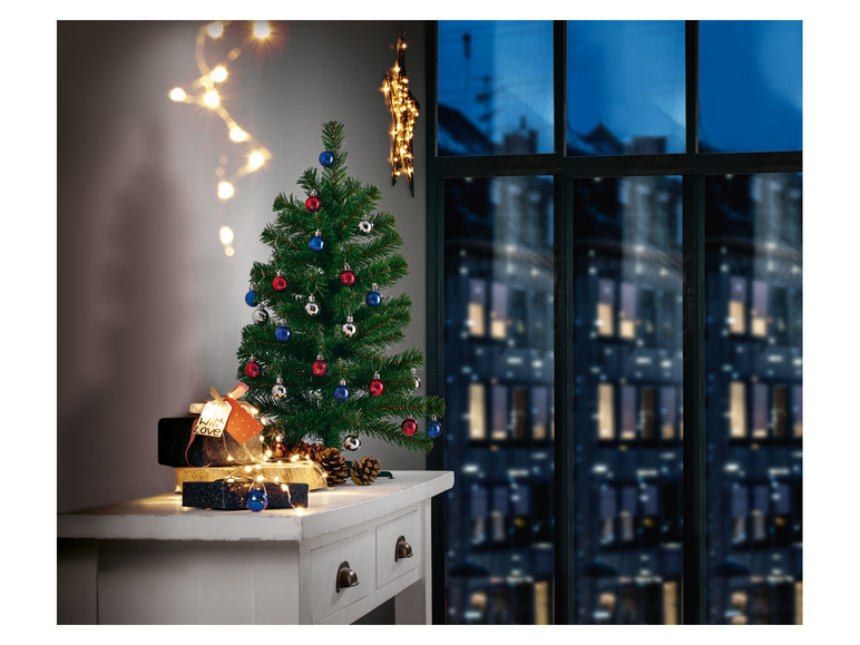 Een kerstboom met kerstversiering en lichtjes op een wit tafeltje.