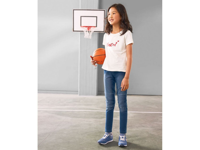 Een meisje met een basketbal, draagt een T-shirt en blauwe jeans