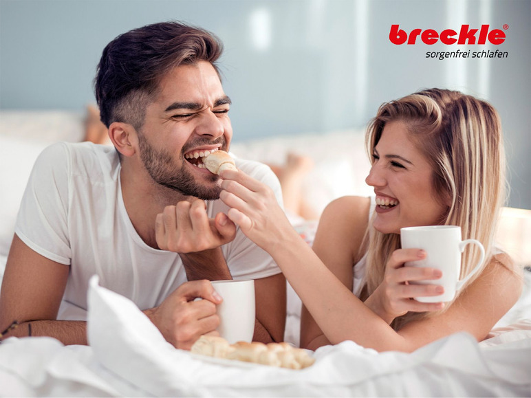 Een stel geniet van koffie en croissants in bed.