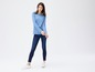 Een vrouw in een blauwe longsleeve en skinny jeans.