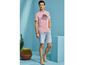 Man draagt een roze T-shirt met Hawaiiaans motief en blauwe denim shorts.