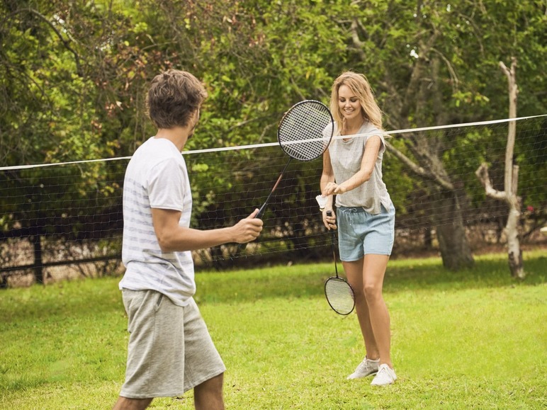 Twee mensen spelen badminton op een grasveld.