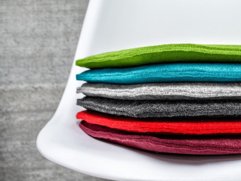 Stapel gekleurde felt zitkussens op een witte stoel.