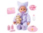 Een pop in een paarse jumpsuit met een teddybeer, fopspeen, fles, bord, bestek en verzorgingsproducten.