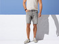 Man draagt grijze denim shorts en witte sneakers.