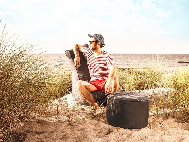 Man zittend in een zwarte loungestoel op het strand met een bijpassende voetenbank.