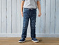 Een kind draagt blauwe jeans en sneakers.