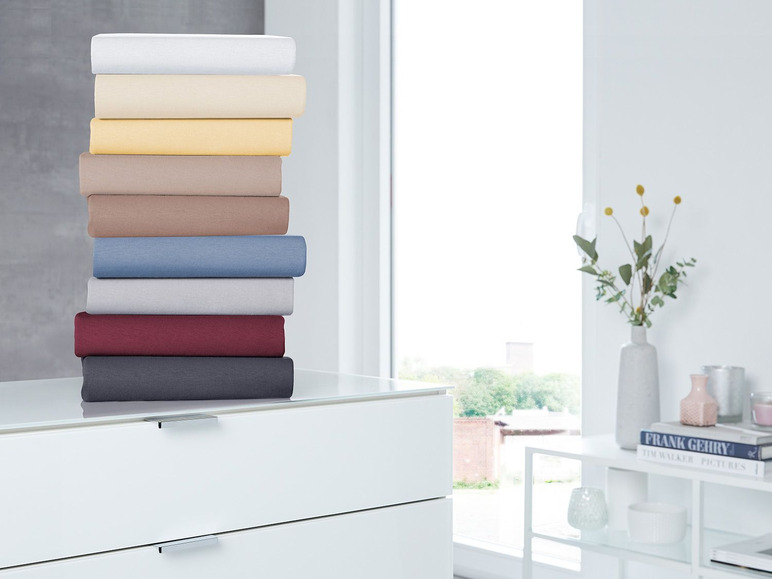 Stapel beddengoed in verschillende kleuren op een witte commode.