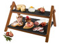 Een houten serveerplateau met twee zwarte leisteenplanken met verschillende soorten charcuterie, kaas en fruit.