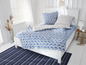 Een wit bed met blauwe schelp-beddengoed en een gestreept vloerkleed.