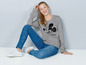 Een vrouw draagt een grijze Mickey Mouse trui, blauwe jeans en witte sneakers.