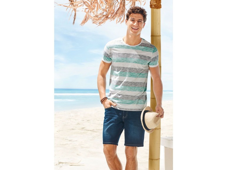 Man in een gestreept T-shirt en jeans shorts op het strand.