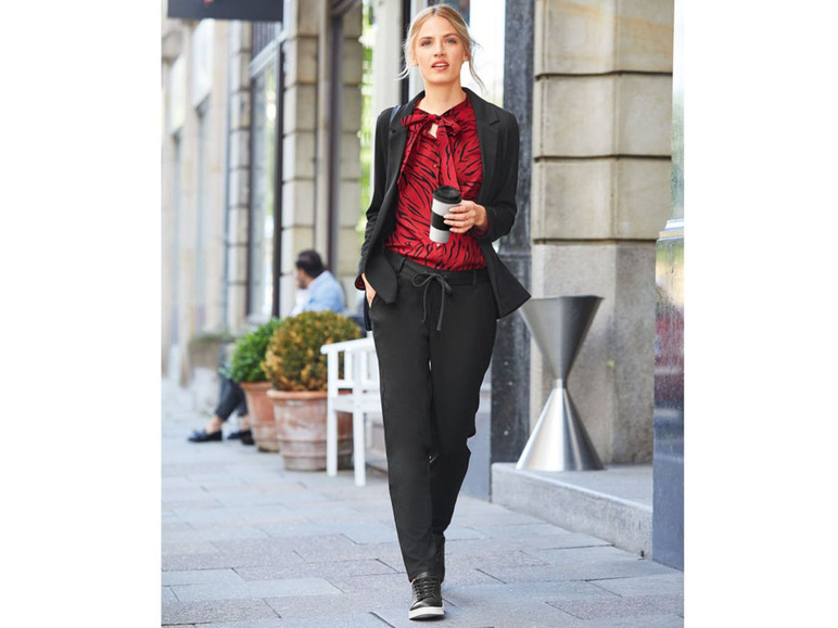 Een vrouw draagt een zwarte blazer, een rode blouse met luipaardprint en zwarte broek.