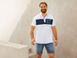 Man draagt een wit poloshirt met blauwe details en een blauwe denim short.