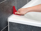Een hand gebruikt een rood gereedschap om kit rond een badkuip te gladstrijken.