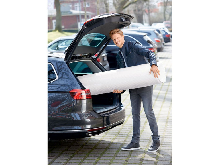 Een man laadt een matras in de kofferbak van een Volkswagen.