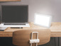 Een laptop en een lichttherapie lamp op een houten bureau.