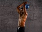 Een man in trainingsbroek die een blauwe kettlebell omhoog houdt
