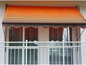 Een oranje en bruin gestreept zonnescherm boven een balkon.